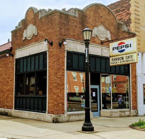 A brick building with a sign for Rainbow Cafe, featuring a Pepsi logo, and a vintage streetlamp outside.