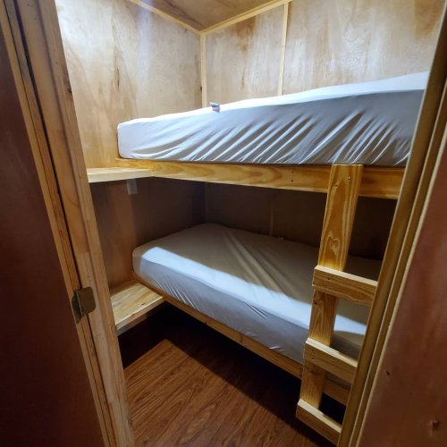 A small room with wooden walls featuring a bunk bed and a shelf, with a clean, minimalist design.