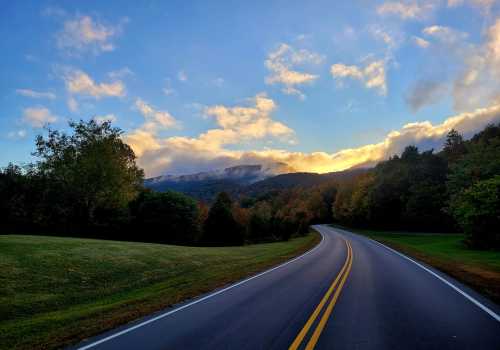 A winding road through lush greenery, with mountains and a colorful sky in the background.