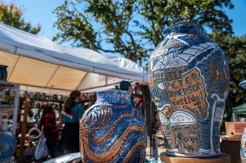 Colorful pottery displayed at an outdoor festival, with a tent and people in the background.