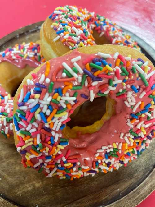 Three colorful donuts with pink icing and vibrant sprinkles on a wooden plate.