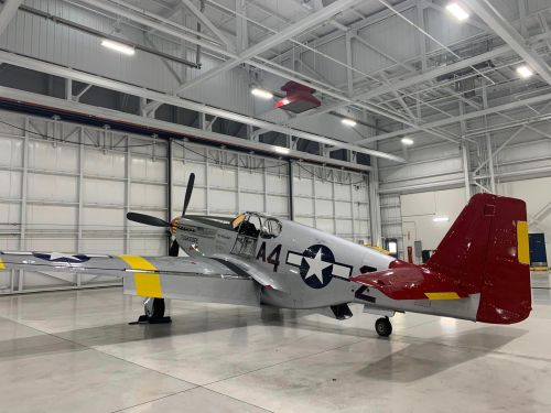 A vintage military airplane with a silver body and red tail, parked inside a spacious hangar.