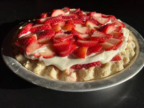 A freshly baked pie topped with sliced strawberries and creamy filling, resting in a silver pie dish.
