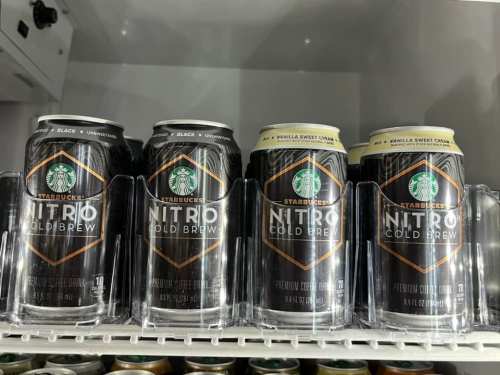 Four cans of Starbucks Nitro Cold Brew, featuring black and vanilla sweet cream flavors, displayed in a refrigerator.