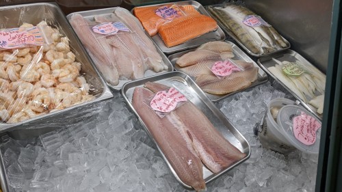 A display of various seafood on ice, including shrimp, salmon, and different fish fillets, with price tags.