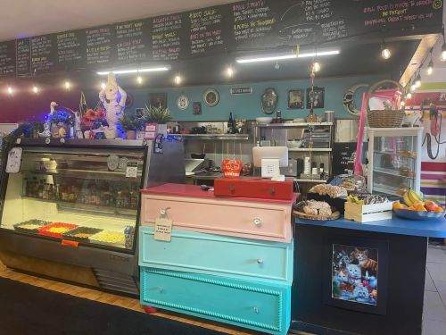 A cozy café interior featuring a colorful display case, vintage decor, and a chalkboard menu overhead.