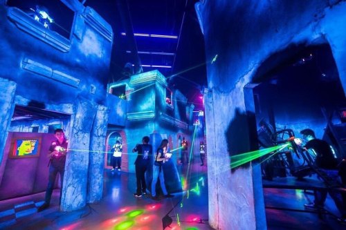 A vibrant laser tag arena with colorful lights, players navigating through futuristic structures and laser beams.