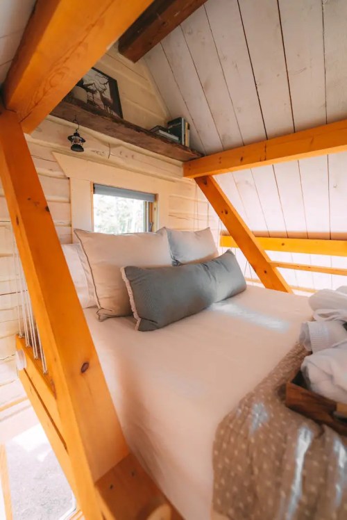 Cozy loft bedroom with wooden beams, a comfortable bed, and decorative pillows, bathed in natural light.