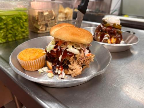 A pulled pork sandwich with coleslaw and barbecue sauce, served with a cornbread muffin on a metal plate.