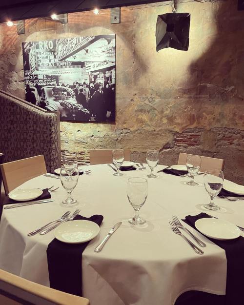 A dining table set with glassware and cutlery, against a backdrop of a vintage black-and-white photo on the wall.