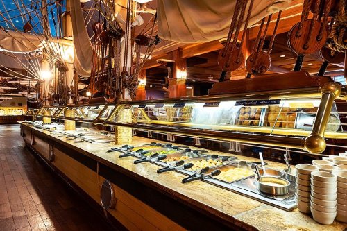A buffet spread featuring various dishes, set in a nautical-themed restaurant with wooden decor and ship elements.