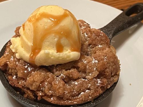 A warm dessert in a cast iron skillet topped with vanilla ice cream and drizzled with caramel sauce.