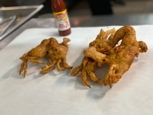 Two large, fried soft-shell crabs on a white paper surface, with a bottle of hot sauce in the background.