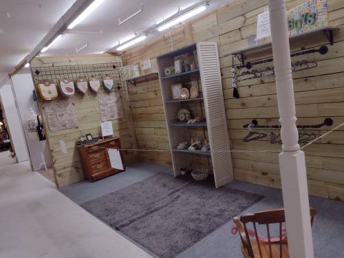A cozy shop interior with wooden walls, shelves, and a small display of home goods and decor items.