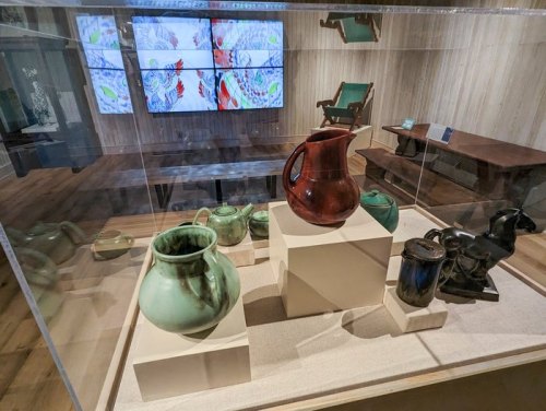 Display of various decorative pots and a horse sculpture in a museum exhibit, with digital screens in the background.
