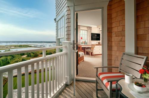 A balcony with a chair and table overlooks a scenic view of a harbor and lush greenery.