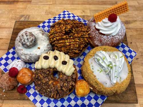 A variety of colorful donuts on a wooden board, featuring toppings like nuts, cream, and fruit, with a checkered background.