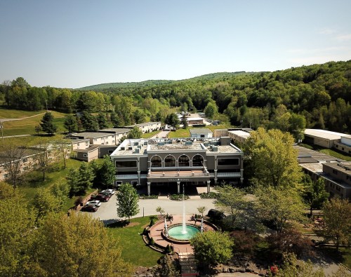 Aerial view of a hotel surrounded by greenery, featuring a fountain and landscaped gardens in a serene setting.