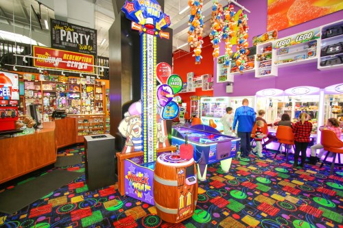 Colorful arcade with various games, including a whack-a-mole machine and claw machines, filled with toys and prizes.