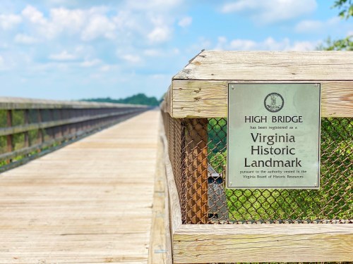 Sign on a wooden bridge railing indicating it is a Virginia Historic Landmark, with a scenic view in the background.