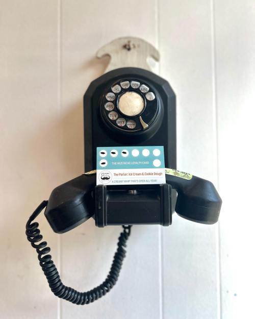 A vintage black rotary phone mounted on a wall, with a loyalty card for an ice cream shop placed on it.
