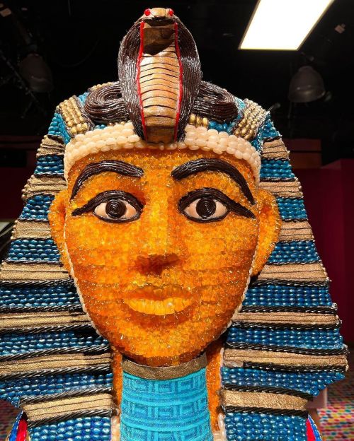 A colorful, beaded sculpture of an ancient Egyptian figure with a cobra headdress and blue-striped hair.