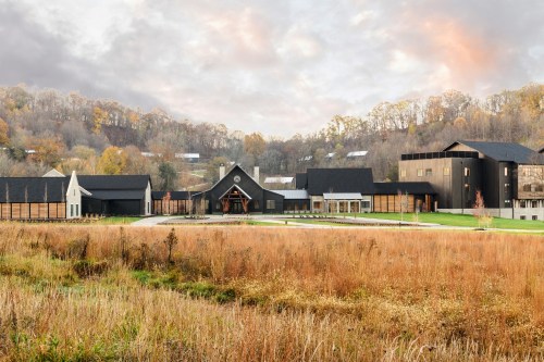 A modern building complex surrounded by autumn foliage and grassy fields under a cloudy sky.