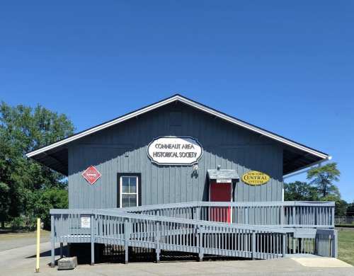A blue building with signs for the Conneaut Area Historical Society and Central System, set against a clear blue sky.