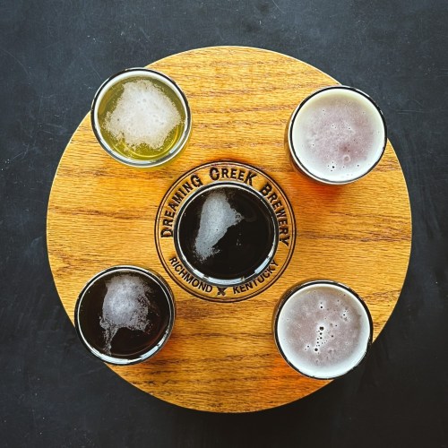 A wooden flight board with four small glasses of different craft beers from Dreaming Creek Brewery.