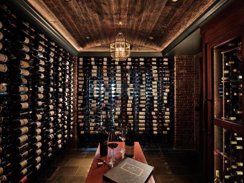A luxurious wine cellar with wooden beams, filled with wine bottles, a table with glasses, and a leather-bound book.