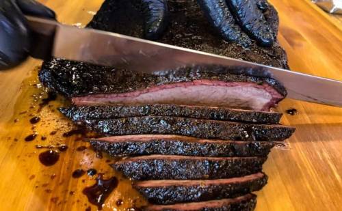 A close-up of a hand slicing a smoked brisket on a wooden cutting board, showcasing its juicy, tender layers.