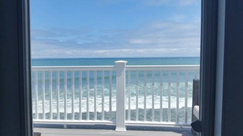 View of a calm ocean with gentle waves, framed by a white railing and a clear blue sky.