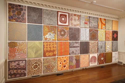 A gallery wall featuring a grid of colorful abstract artworks with circular and linear patterns in various earthy tones.