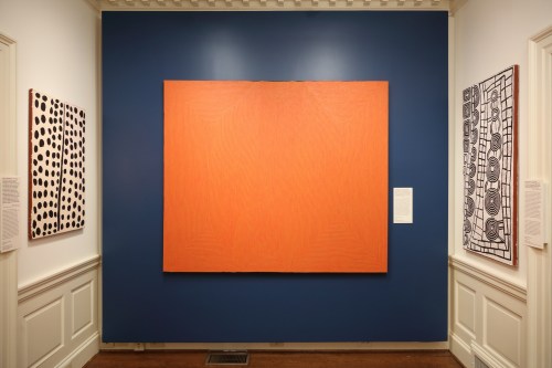 An art gallery featuring an orange canvas on a blue wall, flanked by two patterned artworks.