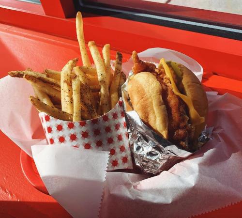 A crispy chicken sandwich with cheese beside a cup of seasoned French fries, all served in a red-themed setting.