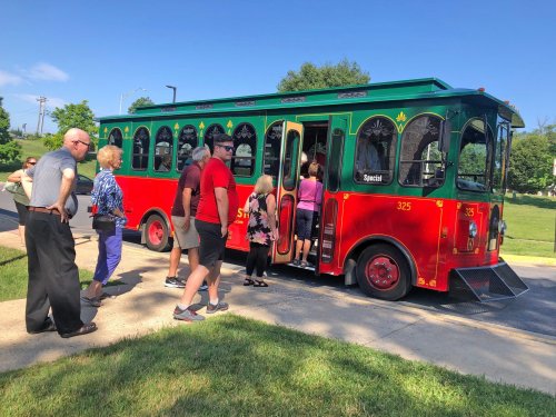 A group of people boarding a colorful red and green trolley on a sunny day.