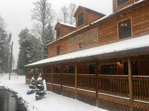 A wooden restaurant and gift shop covered in snow, surrounded by trees, with a sign reading "The Kings Co Mill."
