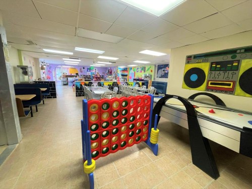 Brightly colored playroom with tables, chairs, and games like Connect Four and air hockey in a cheerful setting.