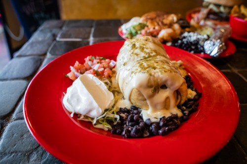 A plate featuring a smothered burrito with cheese, black beans, sour cream, and pico de gallo on a red dish.