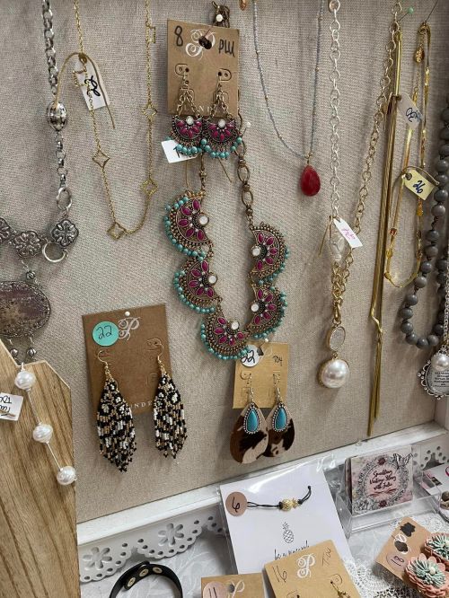 A display of colorful jewelry, including necklaces and earrings, on a fabric background with price tags.