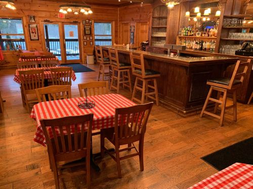Cozy wooden restaurant interior with checkered tablecloths, a bar, and warm lighting.