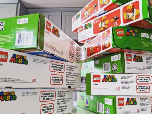 A stack of LEGO Super Mario boxes in various sizes, featuring colorful designs and product information on the sides.