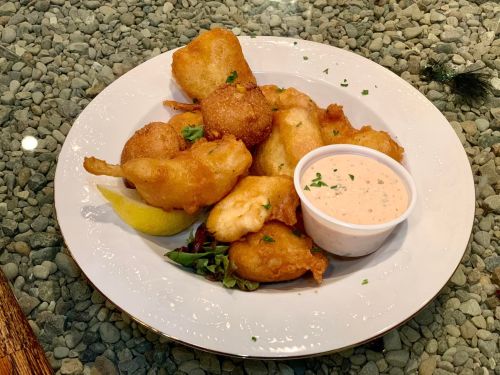 A plate of golden fried seafood and vegetables with a side of dipping sauce and a lemon wedge, garnished with greens.