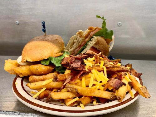 A plate with two sandwiches and a generous serving of loaded fries topped with bacon and cheese.