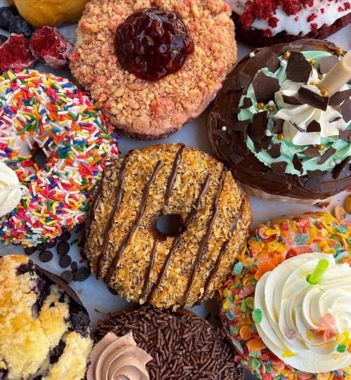 A colorful assortment of gourmet donuts topped with sprinkles, frosting, fruit, and various candies on a white background.