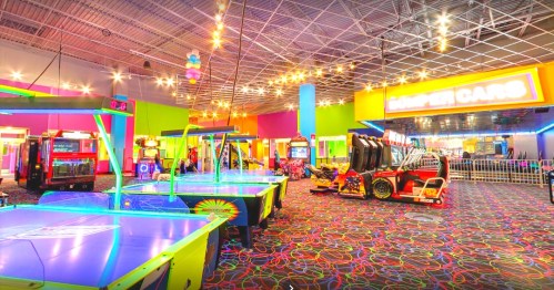 Brightly lit arcade with colorful walls, air hockey tables, and various games, creating a fun, vibrant atmosphere.