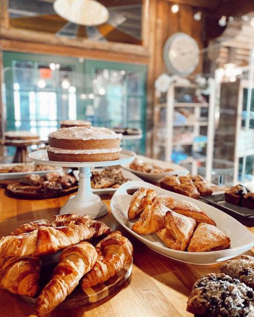 A display of assorted baked goods, including croissants, pastries, and a layered cake, in a cozy café setting.
