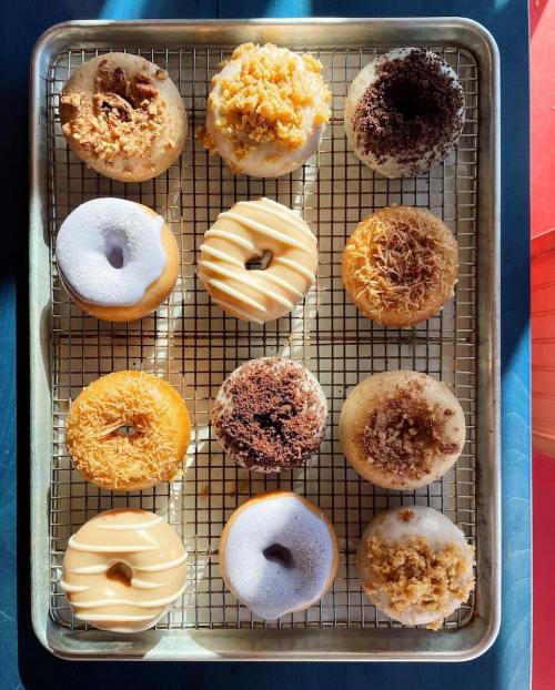 A tray of twelve assorted donuts with various toppings and glazes, arranged in four rows.