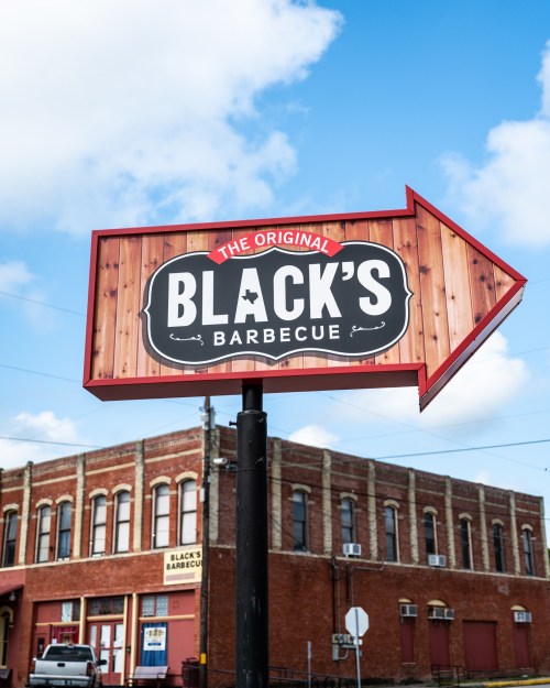 Sign for "Black's Barbecue" with an arrow, set against a blue sky and a brick building in the background.