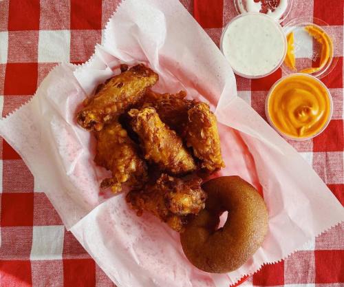 A basket of crispy chicken wings with a donut and dipping sauces on a red and white checkered tablecloth.